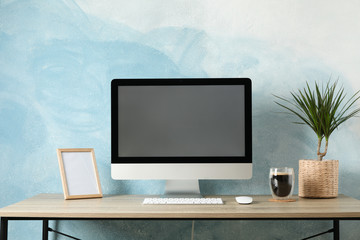 Workplace with computer, plant and glass of coffee on wooden table. Light blue background