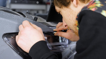 Close up of paint protection film installation on front bumper of modern luxury car. PPF is polyurethane film applied to car surface to protect the paint from stone chips, bug splatter, and abrasion.