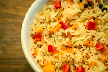 Rice with turmeric or saffron vegetables. Vegetarian lunch with red bell peppers in white bowl on wooden surface.