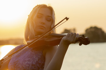 romantic silhouette of young woman with a violin at dawn on river bank, elegant girl playing a...