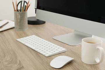 Workplace with computer, keyboard and cup of coffee on wood table, close up