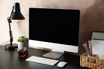 Workplace with computer, plant and lamp on wooden table. Light brown background