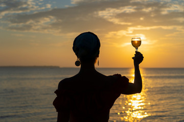 Woman hand holding glass of wine against a beautiful sunset near sea on the tropical beach, close up