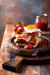 Toast with fried egg, bacon, roasted cherry tomatoes and barbecue relish on the wooden cutting board.