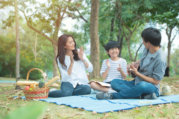 Happy asian family have leisure in public park.Father playing guitar with mother and son clap hands...