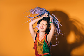 Woman with purple dreadlocks is dancing on an orange background. Hipster woman enjoys life.