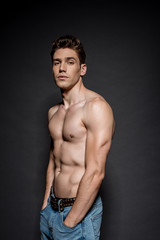 sexy young man with muscular torso posing with hands in pockets on black background