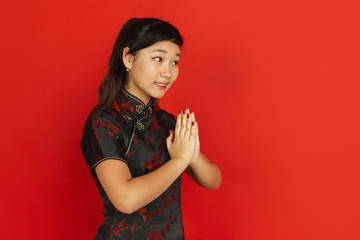 Gesturing, thanks at side. Happy Chinese New Year 2020. Asian young girl's portrait on red background. Female model in traditional clothes looks happy. Celebration, human emotions. Copyspace.