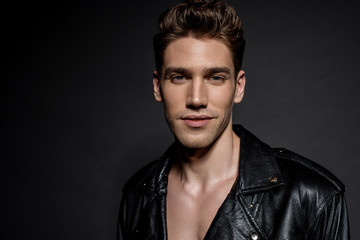Obraz premium smiling handsome sexy young man in biker jacket on black background
