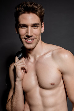smiling sexy young man with muscular torso and biker jacket on black background