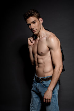 sexy young man with muscular torso and biker jacket on black background