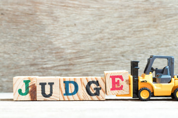 Fototapeta premium Toy forklift hold letter block e to complete word judge on wood background