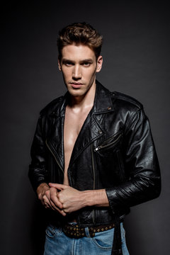 sexy young man with muscular torso in biker jacket and jeans on black background