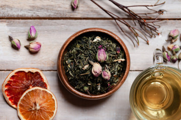 Natural organic dry leaves of green tea with rose flowers and fruits in wooden bowl.  Traditional source of relaxation and detention, atmosphere of spa. Healthy and delicious beverage. Flat lay