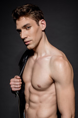 sexy young man with muscular torso and biker jacket on shoulder on black background