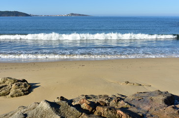 Beach with waves breaking, wet sand, rocks and blue sky. Muxia, Coruña, Galicia, Spain.