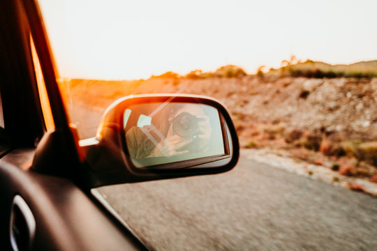 woman taking a self portrait in rear mirror in a car at sunset. travel concept