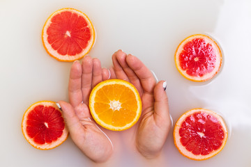 Orange in hands. Slice of red grapefruit citrus fruit in murky muddy milky water around.