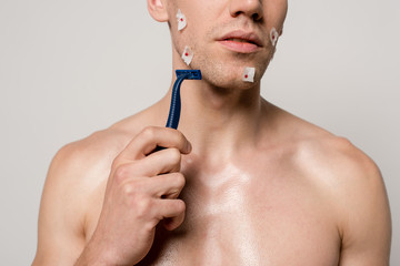cropped view of sexy man with muscular torso and bloody wounds after shaving holding shaver isolated on grey