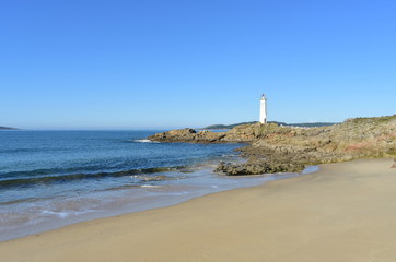 Fototapeta na wymiar Beach with wet sand, rocks and lighthouse with blue sky. Muxia, Coruña, Galicia, Spain.