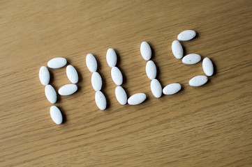 Fototapeta na wymiar PILLS word spelled with white coloured pills on a brown table background