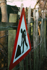 close up shot of men at work sign, roadworks, construction.  trees and wooden fence in background
