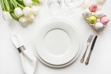 Easter table setting with white tulips, eggs on white table. Top view.