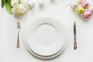 Easter table setting with white tulips, eggs on white table. Top view.