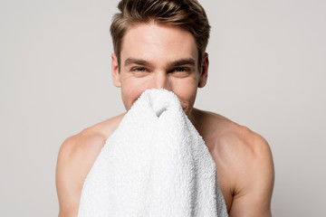 smiling sexy man with muscular torso holding cotton towel in front of face isolated on grey