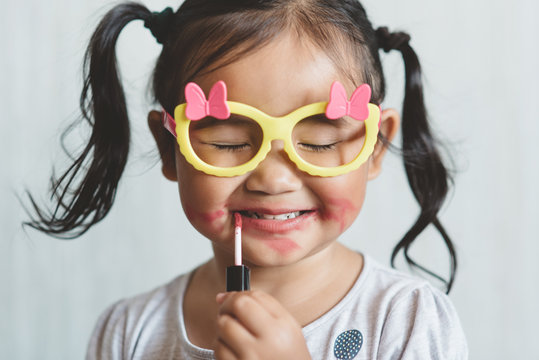 Cute little asian girl playing with toy make up and applying lipstick to her lips. Concept of beauty and childhood