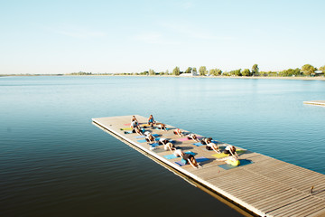 A big group of people attending yoga classes on a pontoon near the lake.