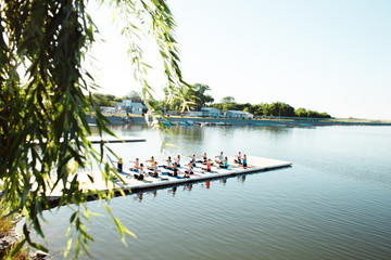 Fototapeta na wymiar A big group of people attending yoga classes on a pontoon near the lake.
