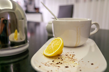 a dirty cup with smudges after tea and the rest of the dessert on a plate, a slice of lemon are on the dining table