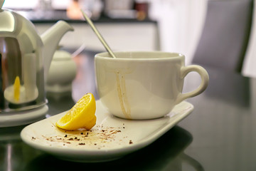 a dirty cup with smudges after tea and the rest of the dessert on a plate, a slice of lemon are on the dining table