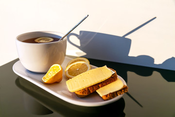 breakfast on the table: hot black tea with lemon, bread toast with cheese, lemon