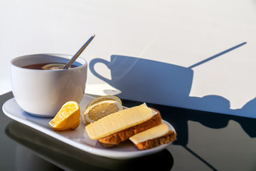 breakfast on the table: hot black tea with lemon, bread toast with cheese, lemon. Soft focus