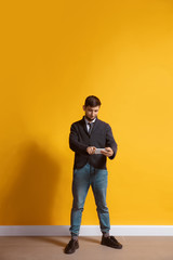Fototapeta na wymiar Pointing on screen. Young caucasian man using smartphone, serfing, chatting, betting. Full length portrait isolated on yellow background. Concept of modern technologies, millennials, social media.