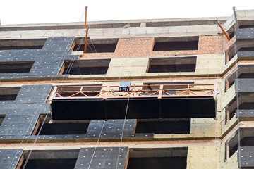 Suspended construction craddle near wall of hightower residentaial building with insulation and...