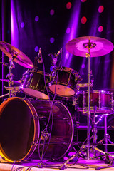 Drum set with bass drum, tom-toms, cymbals and microphones on the stage with violet-red illumination