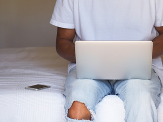Man in casual dress, work on the laptop sitting in the bed at home.