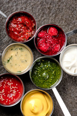 Set of different sauces - ketchup, mayonnaise, barbecue, berry jam, sour cream, pesto, chili, tomato, adzhika, tkemali sauce on black stone background. Top view copy space