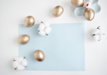 Happy Easter card. Frame with golden Easter eggs and cotton flowers. Copy space for text. Isolated on a pink and white background. Top view.