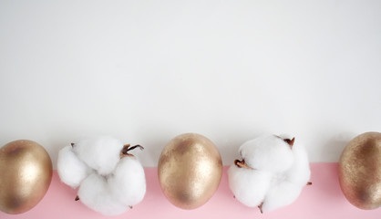 Happy Easter card. Frame with golden Easter eggs and cotton flowers. Copy space for text. Isolated on a pink and white background. Top view.
