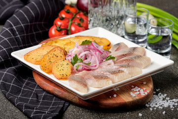 White plate of pieces of pickled herring, chopped chives with fried potato, onion, tomato and cold vodka. Russian traditional cuisine. Close up.