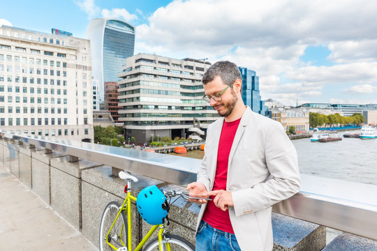 Business Man In London Commuting By Bicycle And Typing On His Smartphone