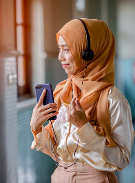 Happy young muslim woman wearing Hijap  listening to the music from her mobile phone, looking through the window and smiling.