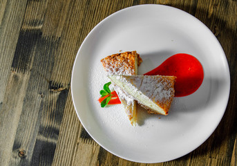 Piece of cake on plate with strawberry sauce on a wooden background