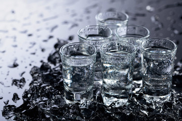 Damp glasses of vodka with ice on a black reflective background.