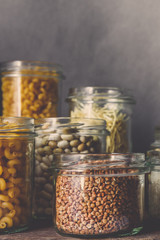 Various raw cereals, grains, beans and pasta for cooking healthy food in glass jars on a wooden...