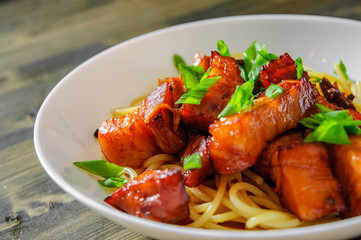 Spaghetti pasta with fried pork in bowl on a wooden background
